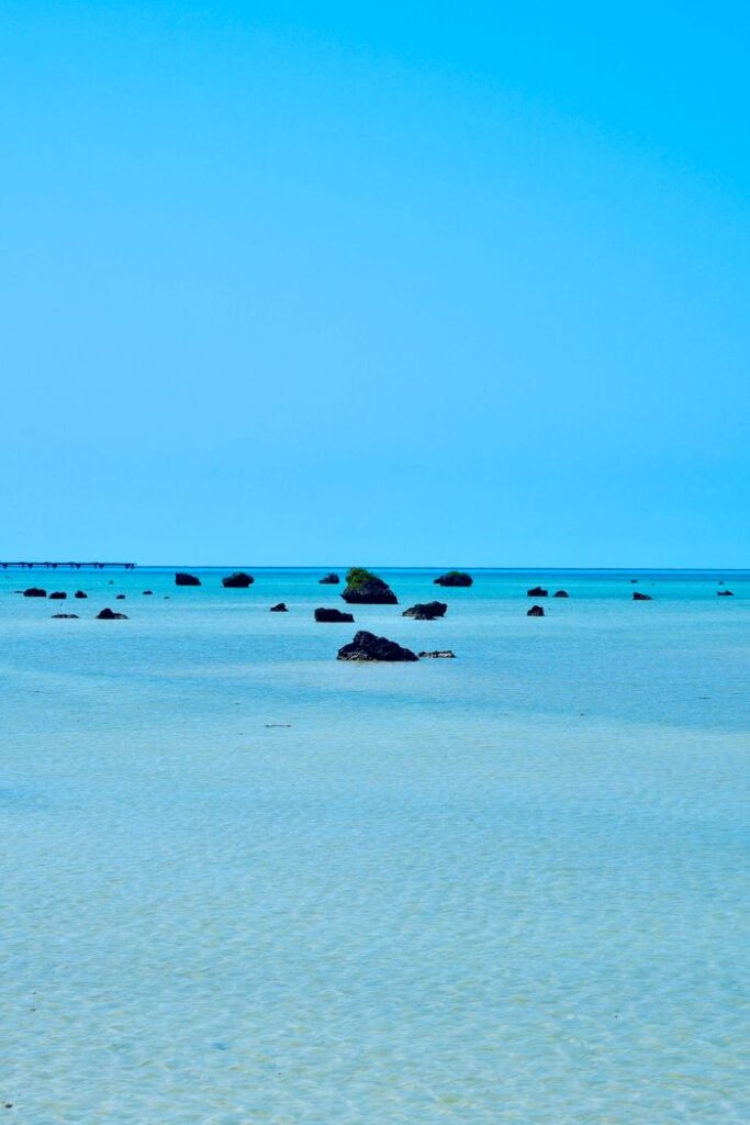 Serene Okinawa beach with clear turquoise waters and scattered rocks.