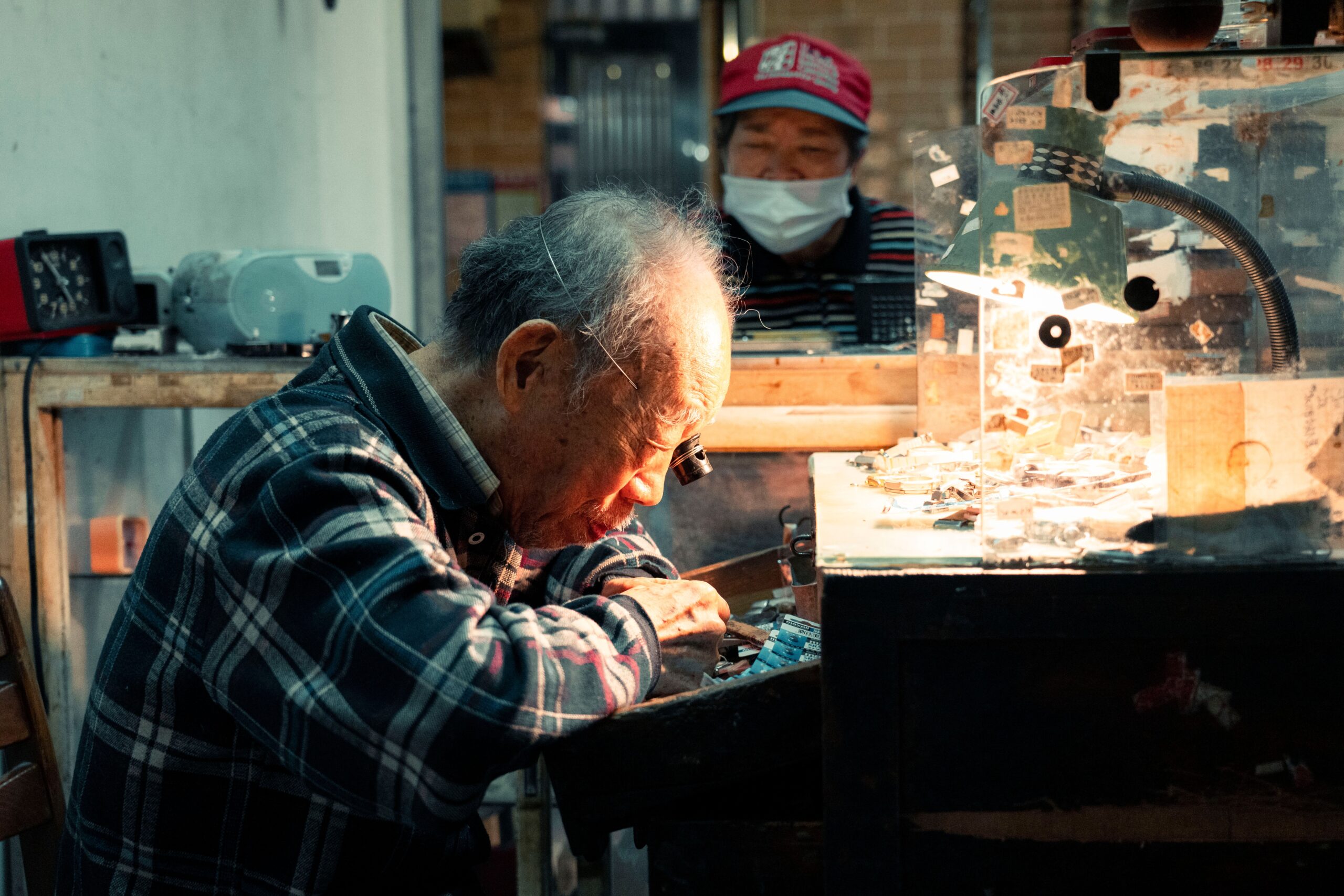 An elderly watchmaker meticulously repairs a watch in a dimly lit workshop, symbolizing dedication to craft.
