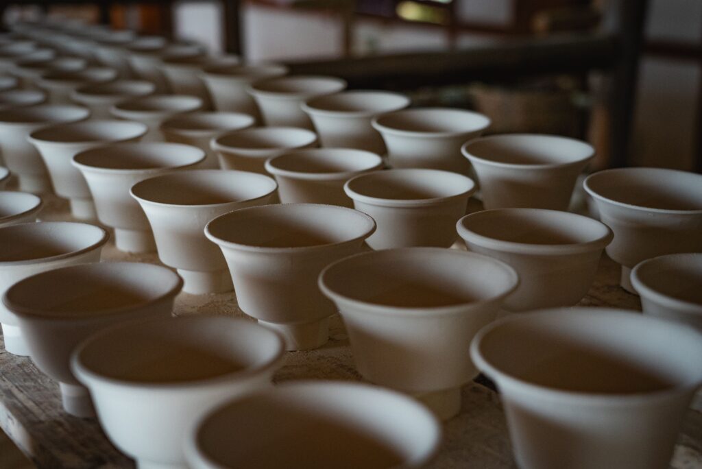 A series of white ceramic cups neatly arranged on a workshop table, showcasing pottery craftsmanship.