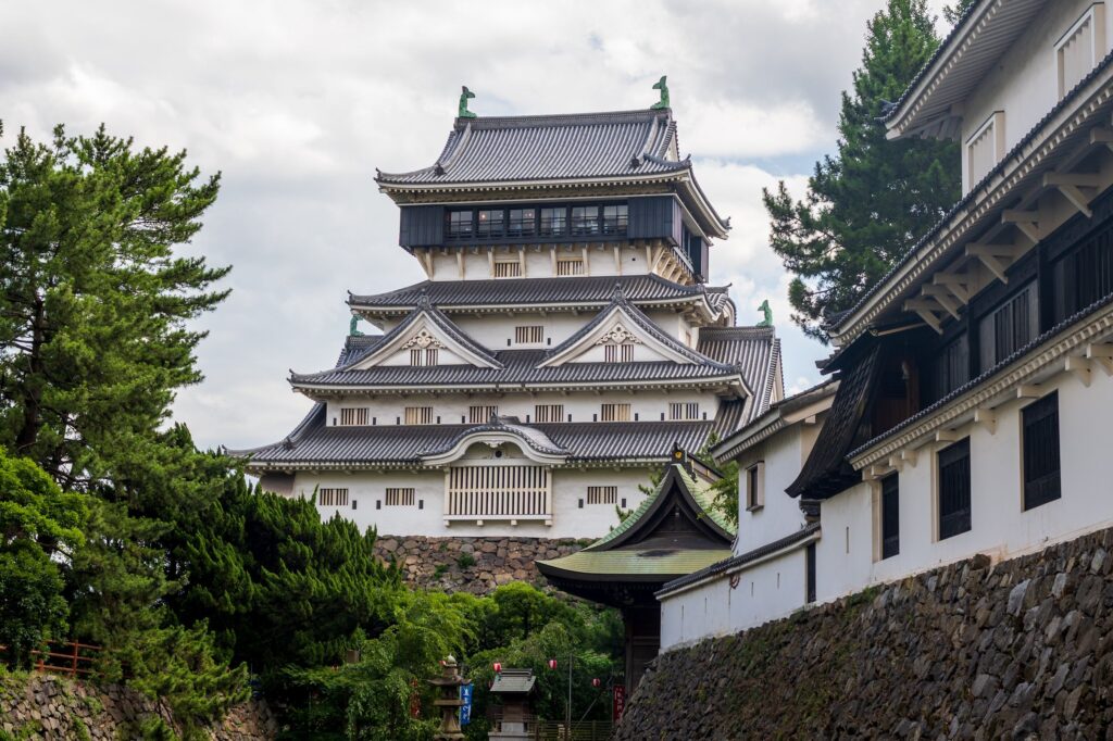 Elegant Japanese castle amidst vibrant greenery under a cloudy sky, showcasing classic architecture.